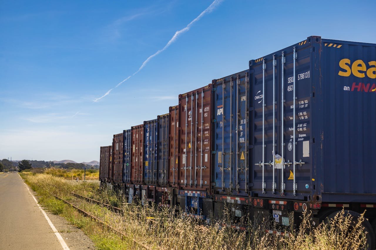 creative-03 Colorful cargo containers on a freight train along a rural railway track under a clear blue sky.